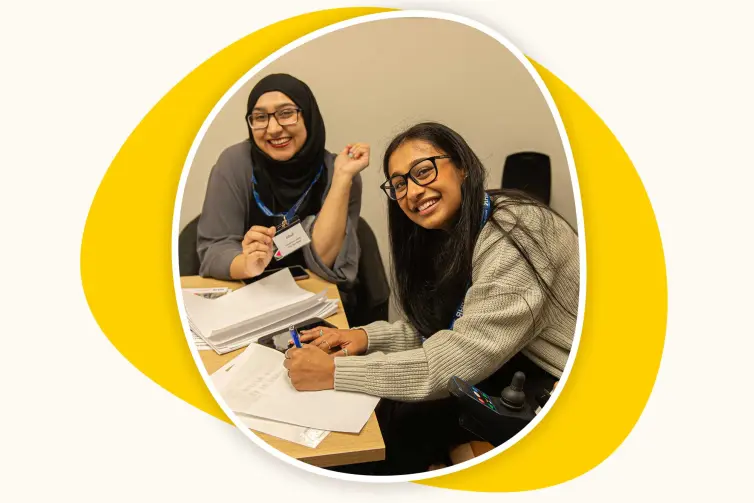 Two young women sat at a desk smiling.